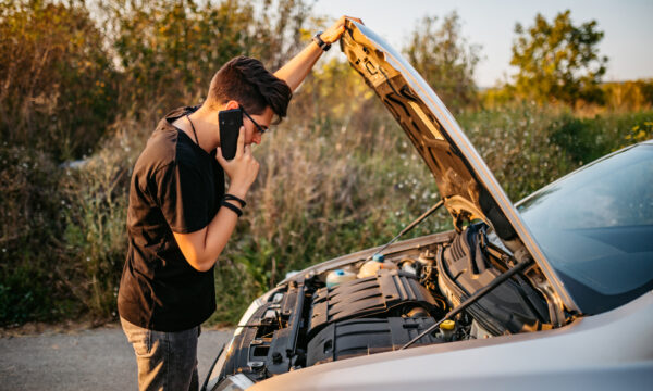 Adult looking at open hood of car and calling roadside assistance